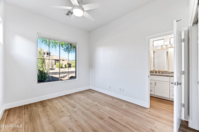 unfurnished bedroom featuring light wood finished floors, baseboards, connected bathroom, ceiling fan, and a sink