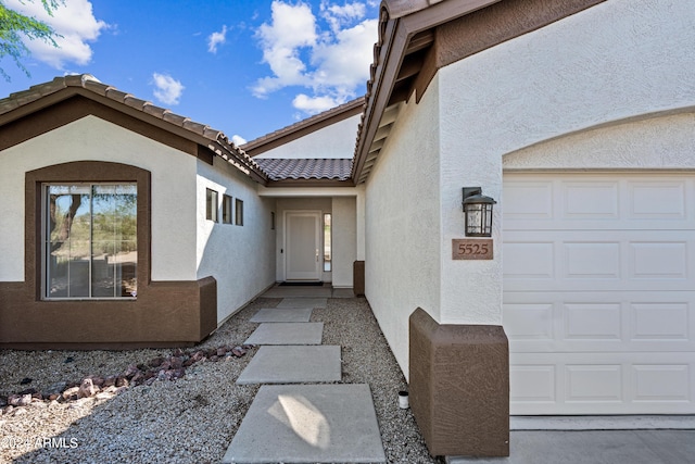 property entrance featuring a garage, a tiled roof, and stucco siding