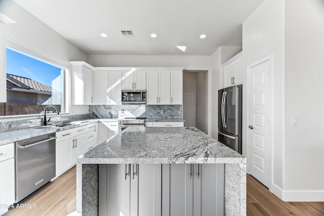 kitchen with a sink, a center island, light wood-style floors, appliances with stainless steel finishes, and decorative backsplash