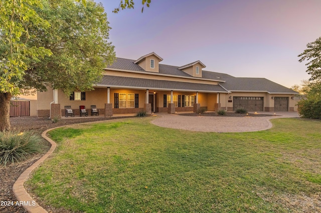 back house at dusk featuring a lawn and a garage