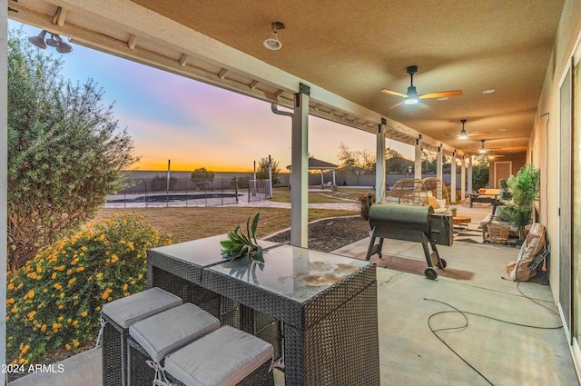 patio terrace at dusk featuring ceiling fan and a pool