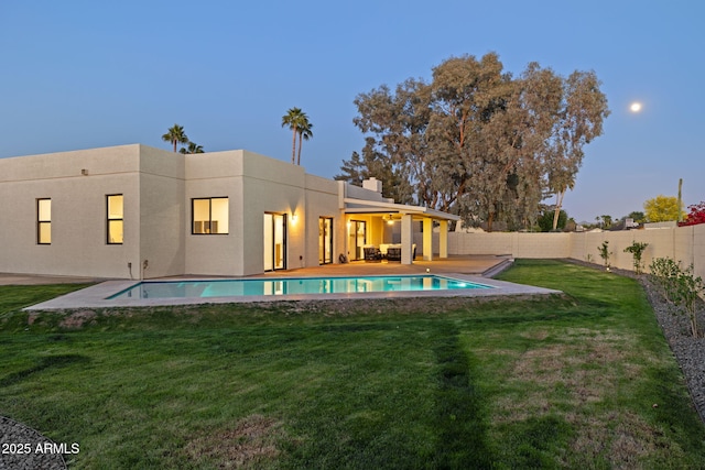 6761 E Juniper Ave, Scottsdale, AZ 85254 - back of property at dusk featuring a fenced in pool, a fenced backyard, stucco siding, and a lawn