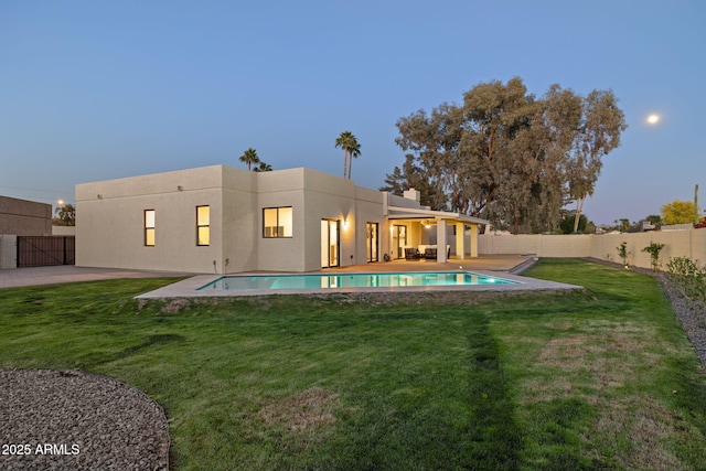 6761 E Juniper Ave, Scottsdale, AZ 85254 - back of property at dusk with a fenced in pool, a fenced backyard, stucco siding, and a lawn