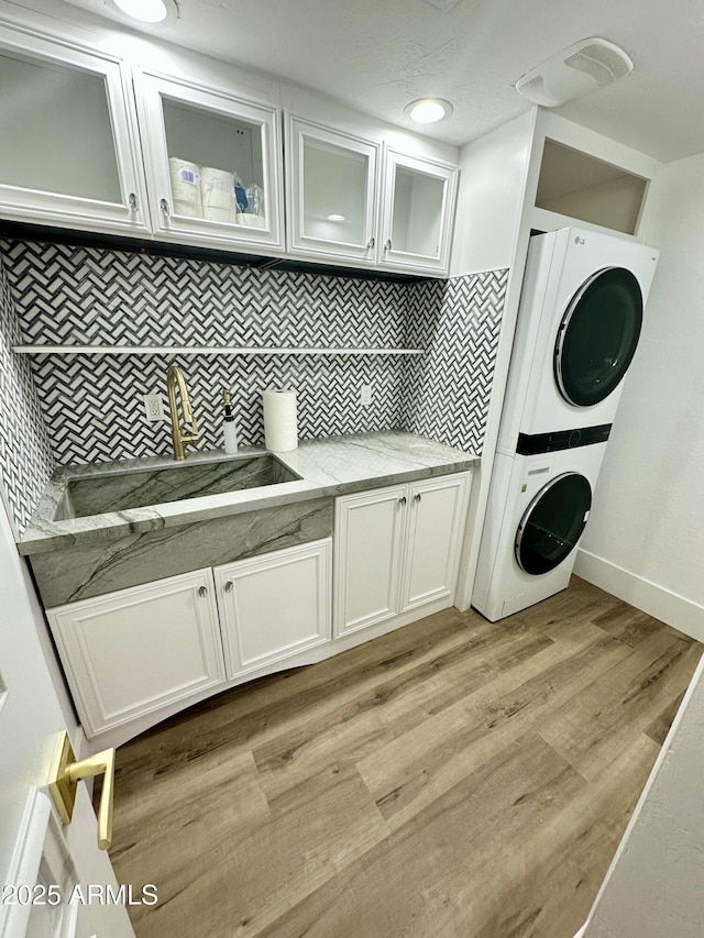 laundry room with a sink, baseboards, light wood-style floors, stacked washer / drying machine, and cabinet space