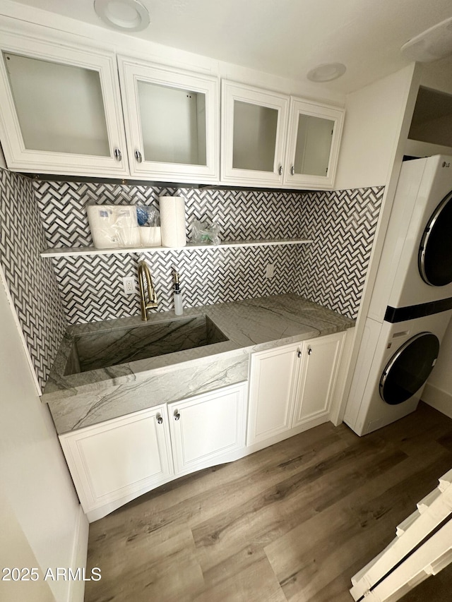 laundry room featuring light wood-type flooring, a sink, and stacked washer / drying machine