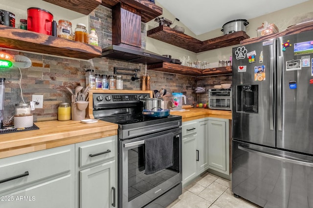 kitchen featuring wall chimney range hood, light tile patterned floors, butcher block counters, backsplash, and stainless steel appliances