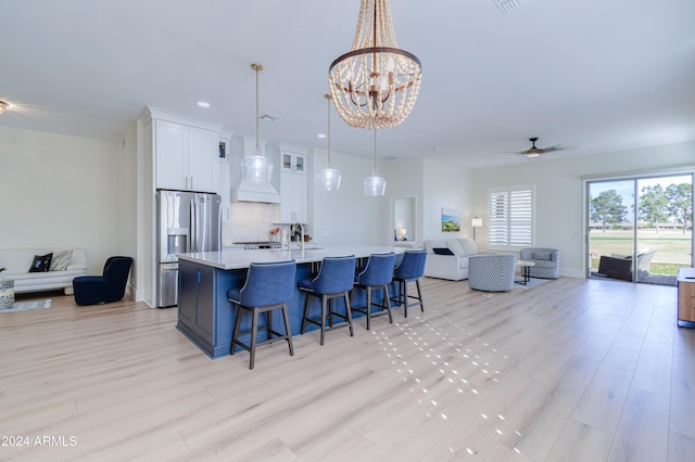 kitchen with a breakfast bar, ceiling fan with notable chandelier, stainless steel fridge with ice dispenser, decorative backsplash, and white cabinetry