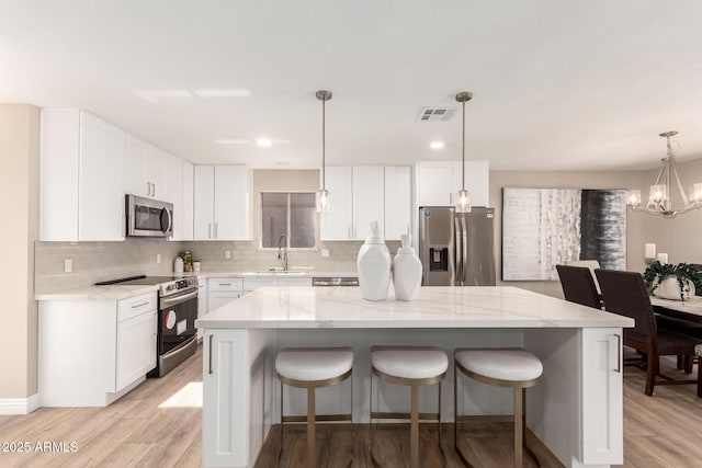 kitchen with stainless steel appliances, a kitchen island, white cabinets, and decorative light fixtures