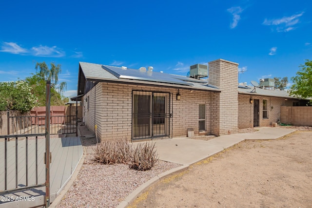 rear view of property featuring brick siding, a fenced backyard, a patio area, and solar panels