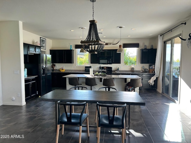 kitchen with a breakfast bar area, decorative light fixtures, a center island with sink, and black appliances