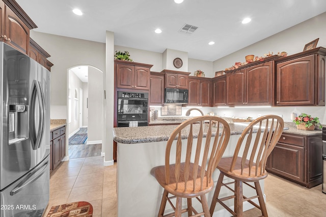 3125 W Desert Ln, Laveen, AZ 85339 - kitchen with black appliances, arched walkways, a kitchen island, light stone countertops, and a kitchen breakfast bar