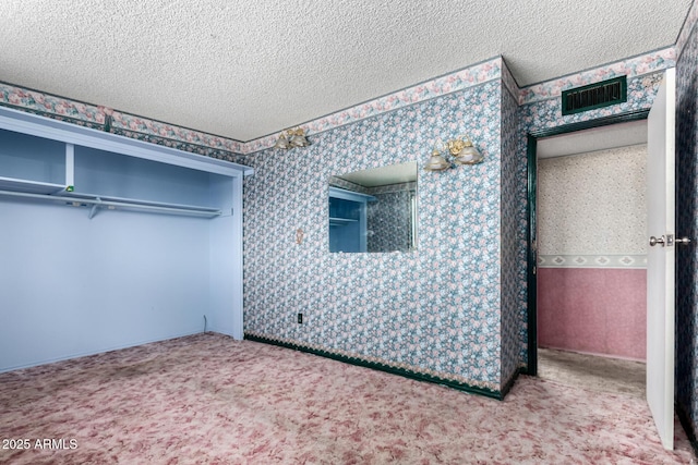 unfurnished bedroom featuring visible vents, a textured ceiling, wallpapered walls, and carpet