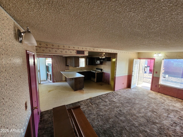 kitchen with light colored carpet, a textured ceiling, wallpapered walls, and electric stove