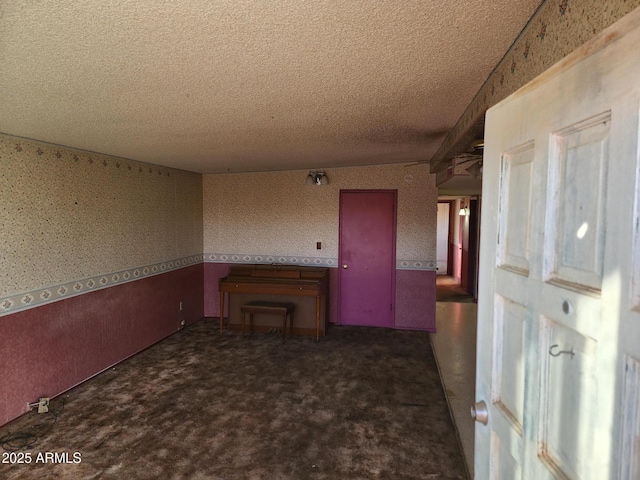 interior space with wallpapered walls, carpet flooring, a wainscoted wall, and a textured ceiling