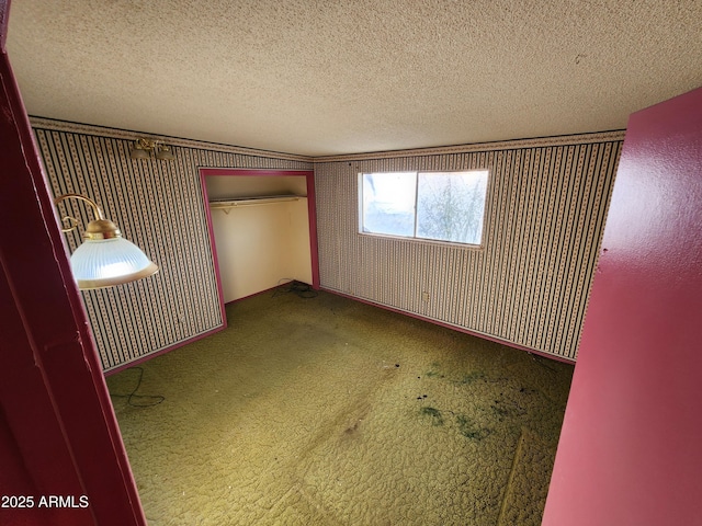 unfurnished bedroom with wallpapered walls, carpet flooring, a closet, and a textured ceiling