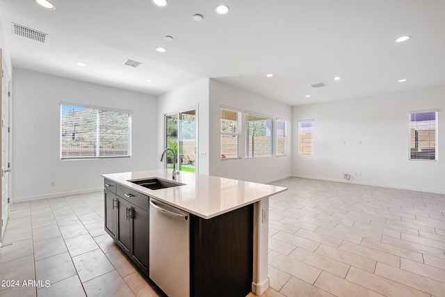 kitchen featuring a kitchen island with sink, sink, light tile floors, stainless steel dishwasher, and dark brown cabinetry