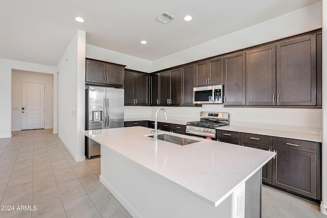 kitchen featuring dark brown cabinetry, light tile floors, an island with sink, stainless steel appliances, and sink