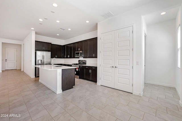 kitchen featuring light tile flooring, a kitchen island with sink, sink, stainless steel appliances, and dark brown cabinets