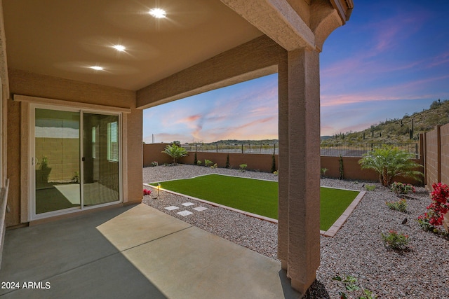 patio terrace at dusk featuring a lawn