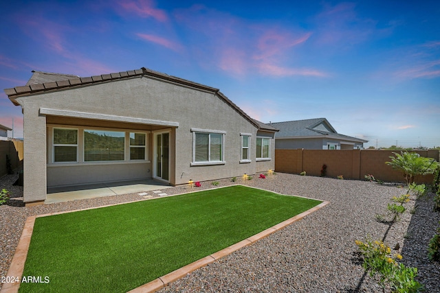 back house at dusk with a yard and a patio