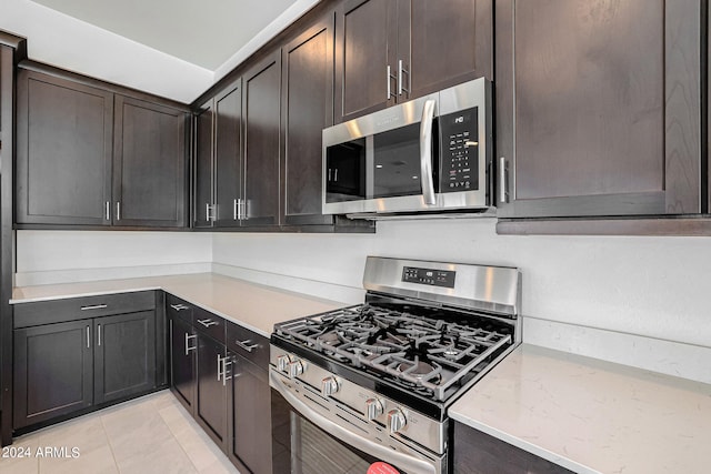 kitchen with appliances with stainless steel finishes, light stone counters, light tile flooring, and dark brown cabinetry