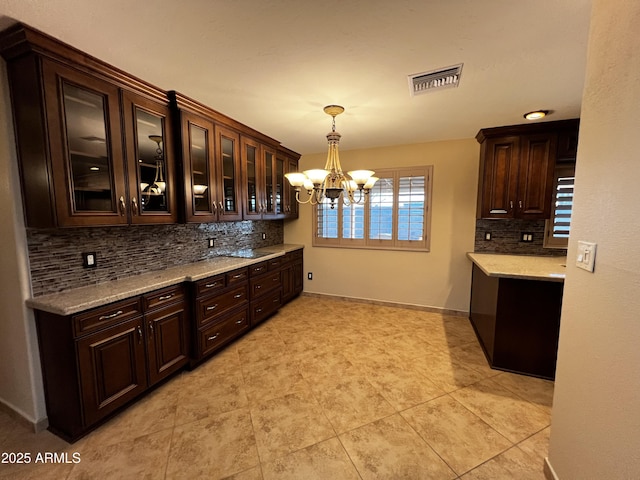 kitchen featuring dark brown cabinets, an inviting chandelier, light stone counters, and decorative light fixtures