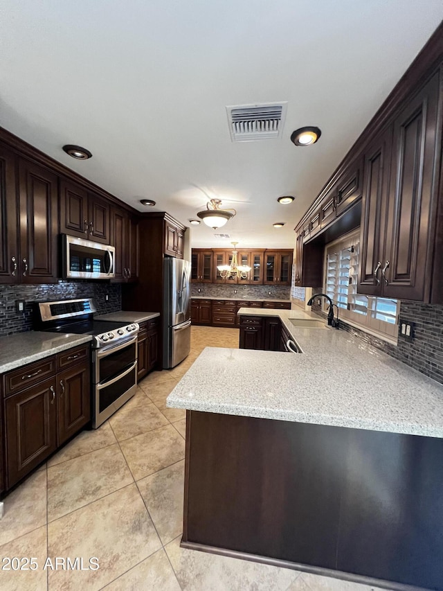 kitchen with sink, appliances with stainless steel finishes, dark brown cabinets, decorative backsplash, and kitchen peninsula