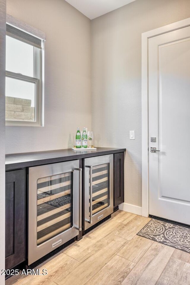 bar with beverage cooler, light wood finished floors, a dry bar, and baseboards