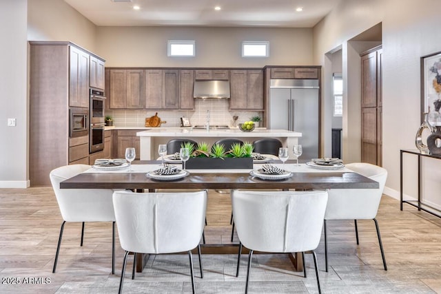 kitchen with under cabinet range hood, built in appliances, light countertops, light wood-type flooring, and decorative backsplash