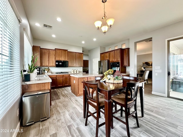 kitchen with light wood-type flooring, sink, black appliances, decorative light fixtures, and an inviting chandelier