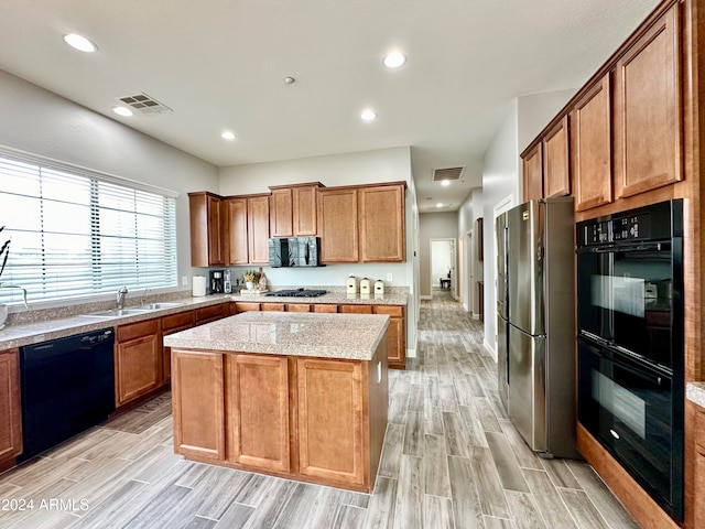 kitchen with black appliances, sink, a kitchen island, light stone countertops, and light hardwood / wood-style floors