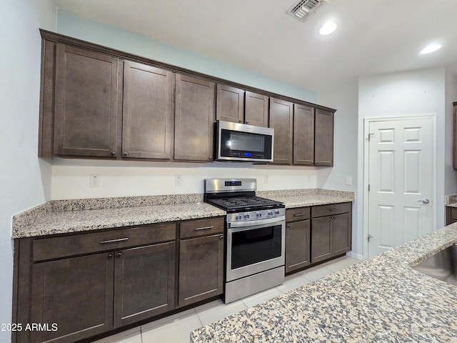 19954 W Moonlight Path, Buckeye, AZ 85326 - kitchen with stainless steel appliances, dark brown cabinetry, light tile patterned floors, light stone counters, and recessed lighting