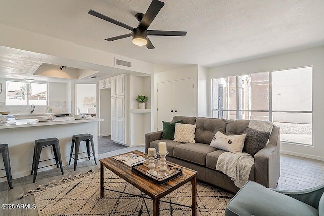 living room with sink, ceiling fan, light hardwood / wood-style flooring, and a textured ceiling