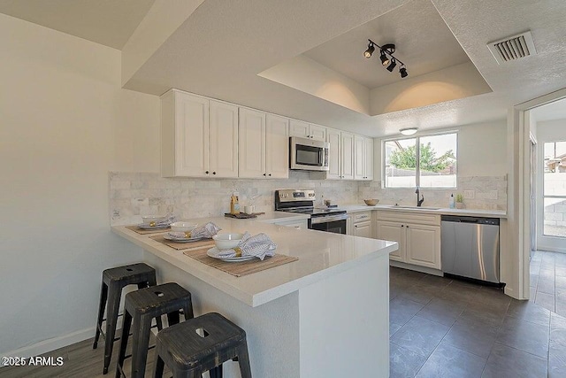 kitchen with appliances with stainless steel finishes, white cabinetry, a kitchen breakfast bar, kitchen peninsula, and a tray ceiling