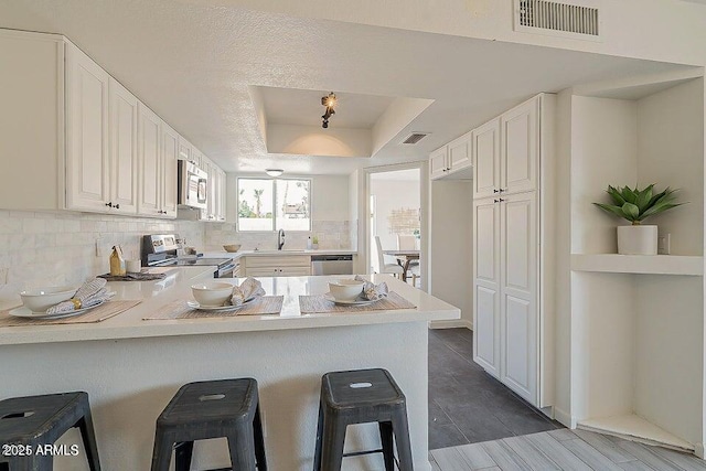 kitchen with white cabinets, appliances with stainless steel finishes, a kitchen breakfast bar, kitchen peninsula, and a raised ceiling