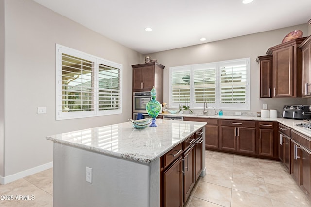 kitchen with sink, light stone counters, a kitchen island, and plenty of natural light