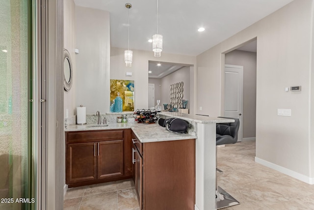 interior space featuring kitchen peninsula, light stone countertops, sink, a kitchen bar, and pendant lighting