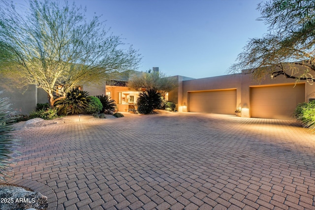 pueblo-style house with an attached garage, decorative driveway, and stucco siding