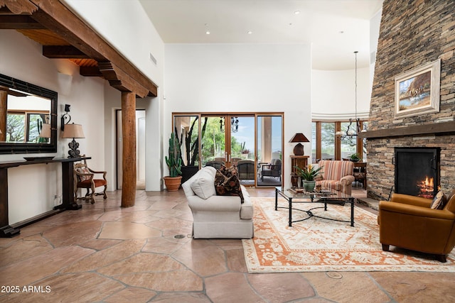 living area featuring stone tile floors, a stone fireplace, a wealth of natural light, and a towering ceiling