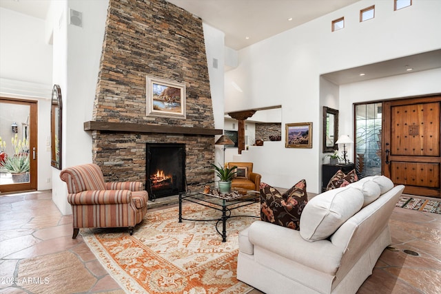 living area with stone tile flooring, visible vents, a towering ceiling, a fireplace, and recessed lighting