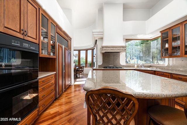 kitchen with dobule oven black, decorative backsplash, brown cabinets, and light wood-type flooring