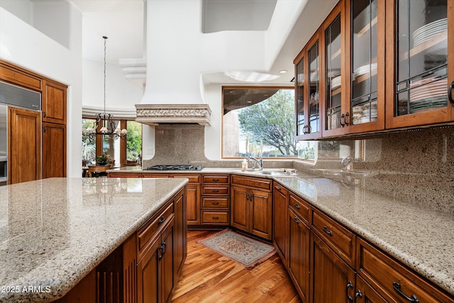 kitchen featuring backsplash, light stone countertops, a sink, stainless steel gas stovetop, and light wood-style flooring
