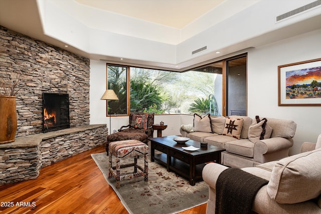 living area with visible vents, wood finished floors, and a stone fireplace