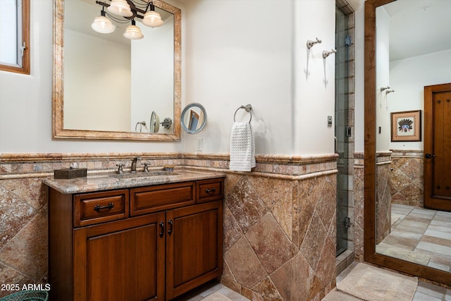 full bath with vanity, a shower stall, a wainscoted wall, and tile walls