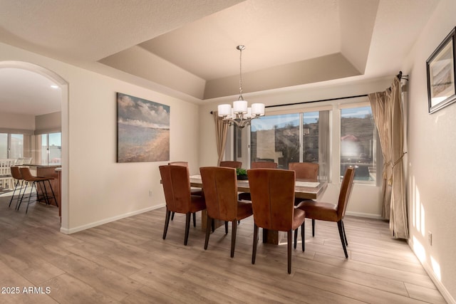 dining area with a notable chandelier, light wood-type flooring, and a tray ceiling