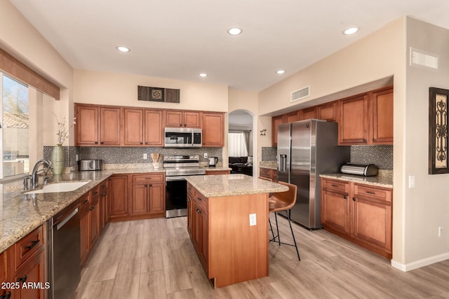 kitchen featuring sink, light hardwood / wood-style floors, a kitchen island, a breakfast bar, and appliances with stainless steel finishes