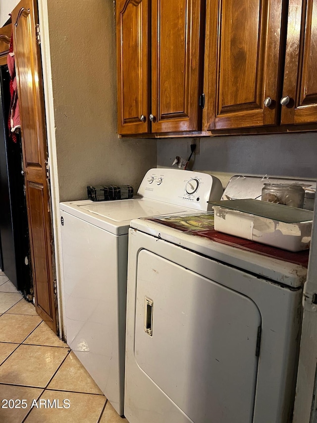 clothes washing area featuring washing machine and dryer, light tile patterned floors, and cabinets