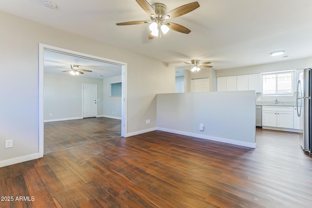 unfurnished living room with dark wood-type flooring, a sink, and baseboards