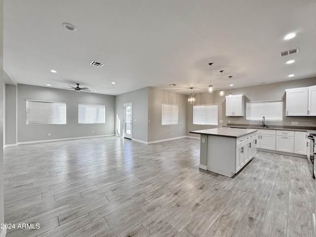 kitchen with white cabinetry, sink, pendant lighting, a kitchen island, and ceiling fan with notable chandelier