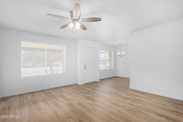 spare room featuring ceiling fan with notable chandelier and light wood-type flooring